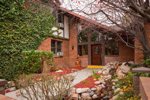 A landscaped pathway leads to the wooden door of a vine-covered red brick house with vaulted ceilings.