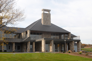A gray and blue house with large windows and rock accents sits on an open green lawn.