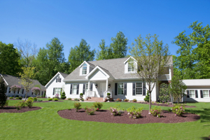 A ranch style, two-story white home sits on a small hill with a landscaped open yard.