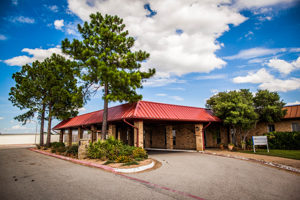 An asphalt driveway leads to a one-story brick building with a red roof.