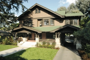 A concrete path surrounded by grass on both sides leads to a brown two-story house with a green roof.