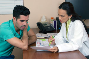 A woman uses a green pen to point something out on a piece of paper to a man who sits leaning forward looking at the paper